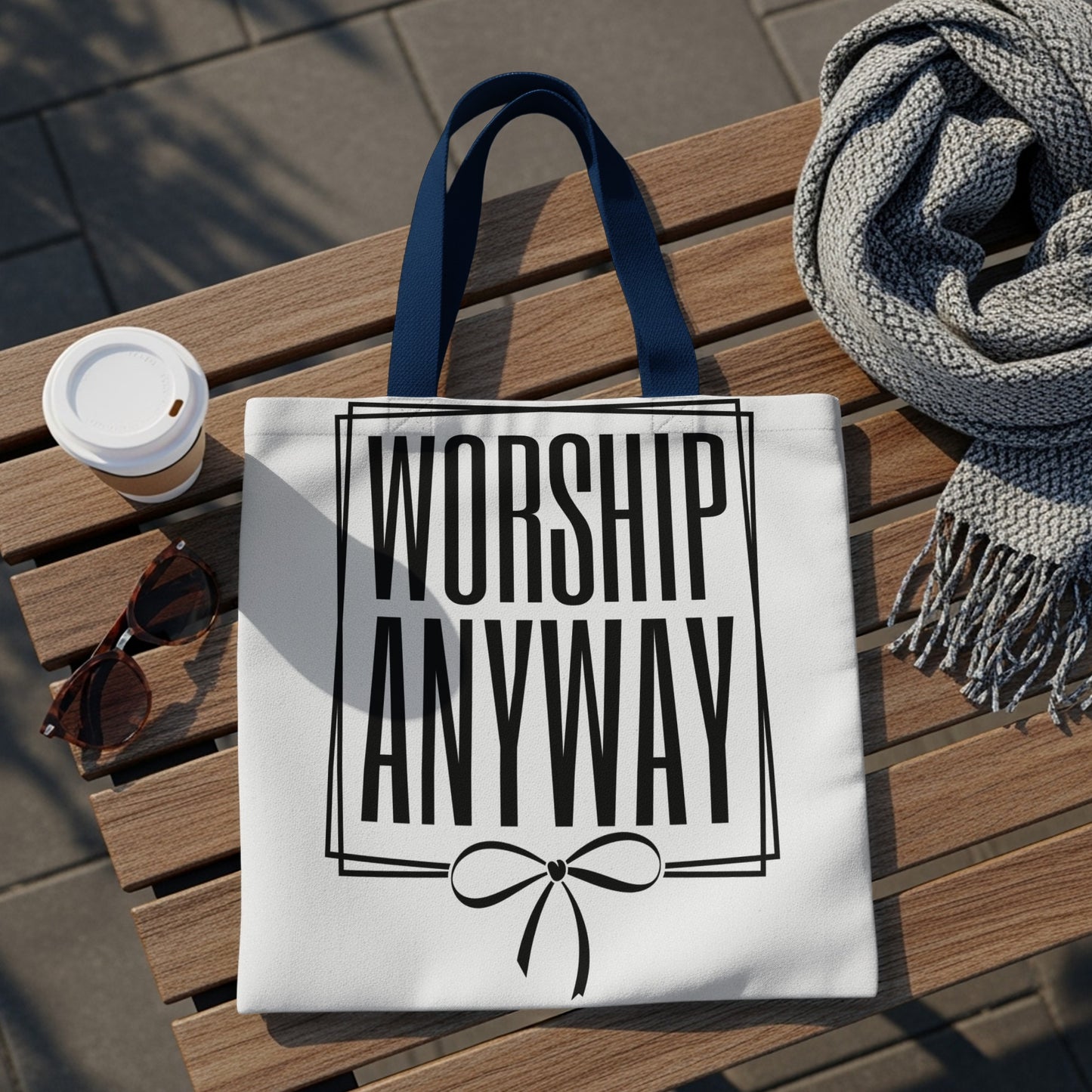 White tote bag with "WORSHIP ANYWAY" text in black, framed by a box and bow.