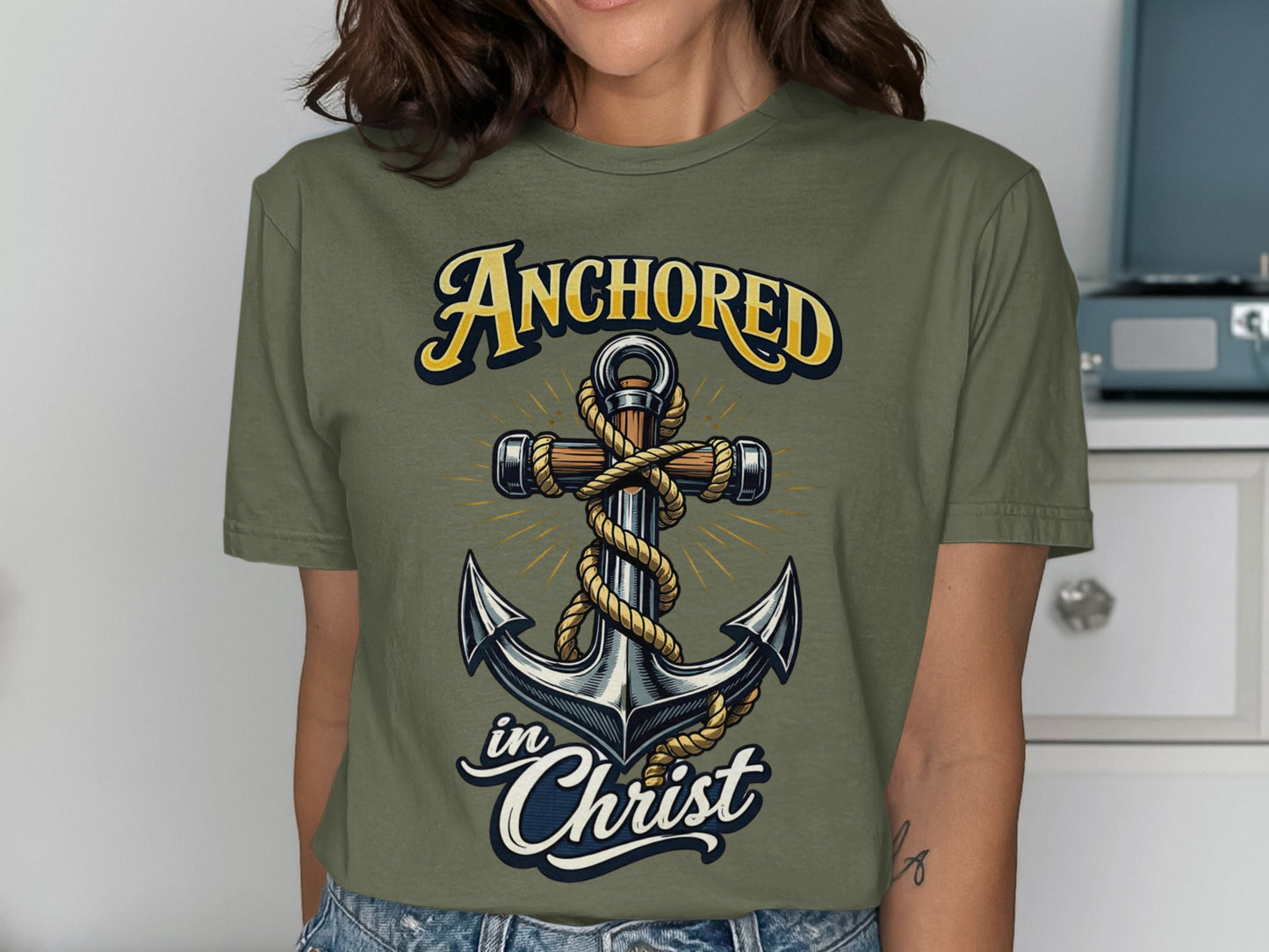 Olive green t-shirt with a graphic of an anchor, rope, and text "Anchored in Christ".