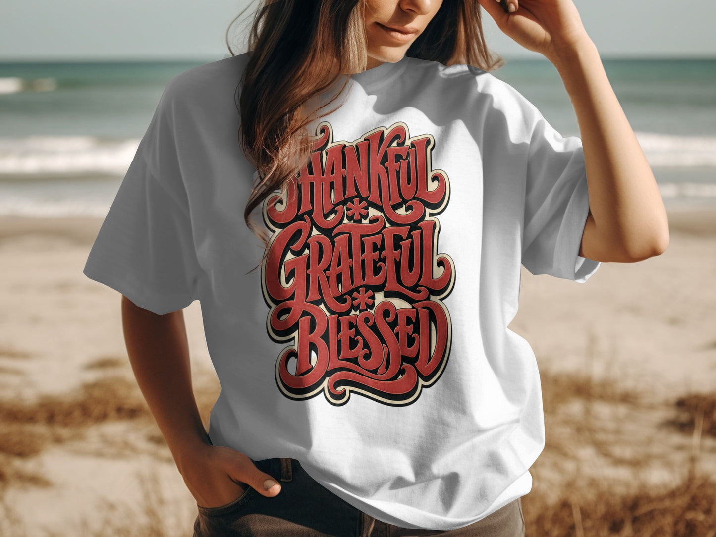White t-shirt with red text "Thankful Grateful Blessed" on a beach background.