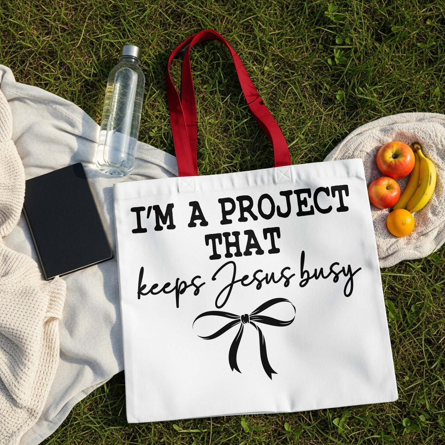 White tote bag with red handles, featuring text and a bow.
