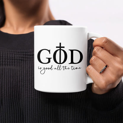 White mug with black text "GOD is good all the time" and cross symbol.