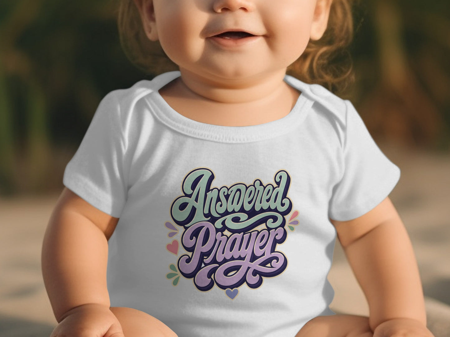 Baby wearing a white onesie with "Answered Prayer" in pastel lettering.