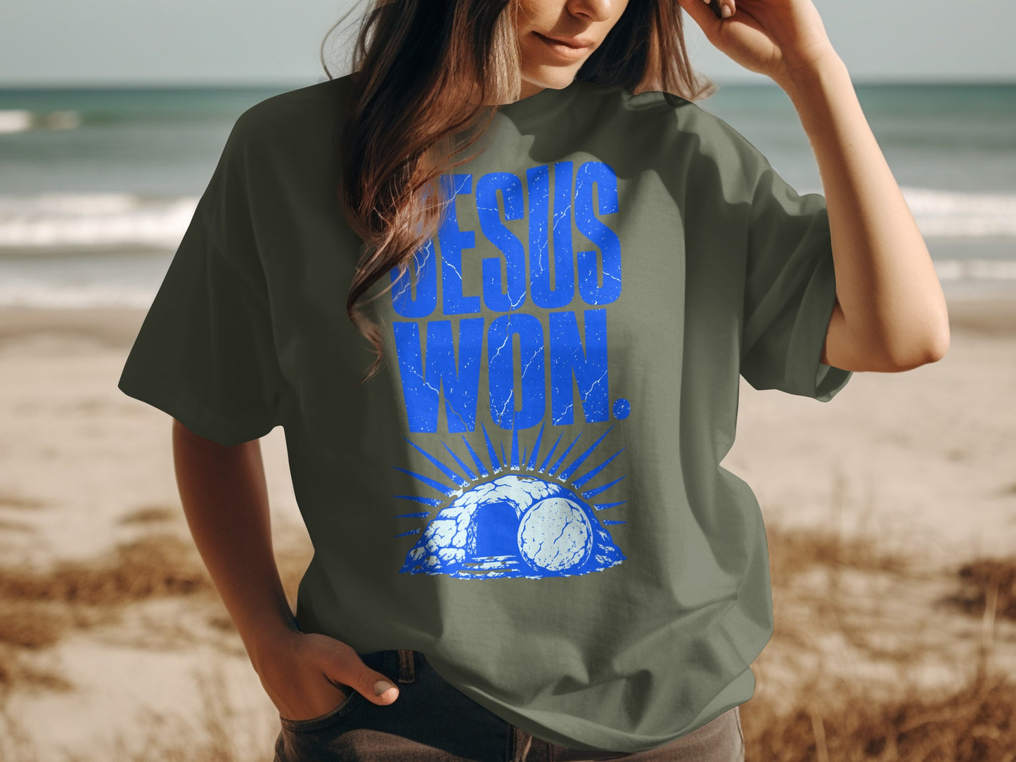 T-shirt with blue "Jesus Won" text over a tomb graphic on a beach.