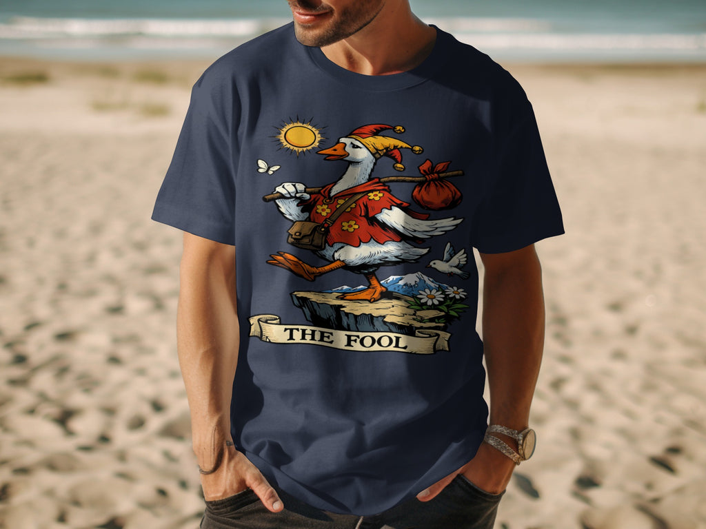 T-shirt with graphic of a goose dressed as "The Fool" tarot card on cliff overlooking beach.
