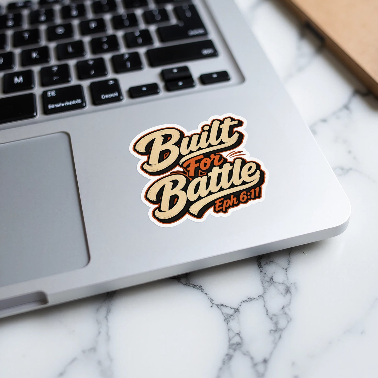 Sticker with "Built For Battle Eph 6:11" text on a laptop keyboard.