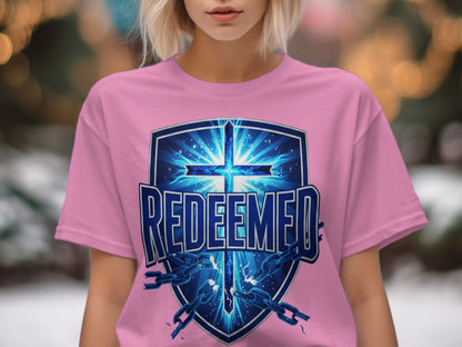 Pink t-shirt with blue shield graphic featuring a cross, broken chains, and text "REDEEMED".
