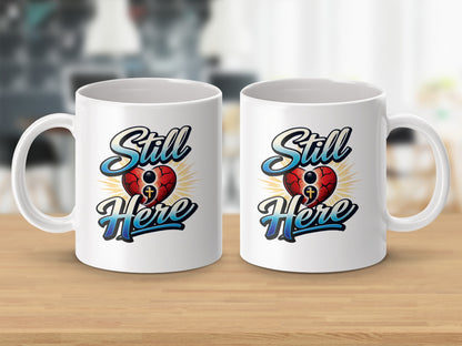 Two white mugs featuring a red cracked heart with a cross and the text "Still Here".