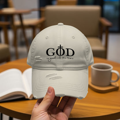 Distressed light-colored baseball cap with "GOD is good all the time" text.