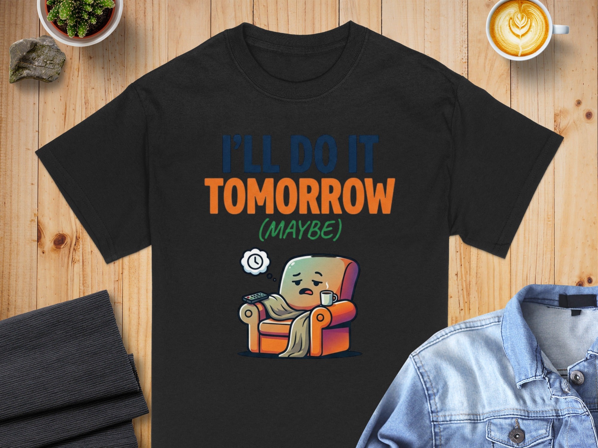 Black t-shirt with text "I'LL DO IT TOMORROW (MAYBE)" and cartoon of armchair.