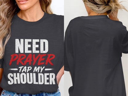 Dark gray t-shirt with white text reading "NEED" and "SHOULDER", red text reading "PRAYER", and hyphenated text reading "TAP MY".
