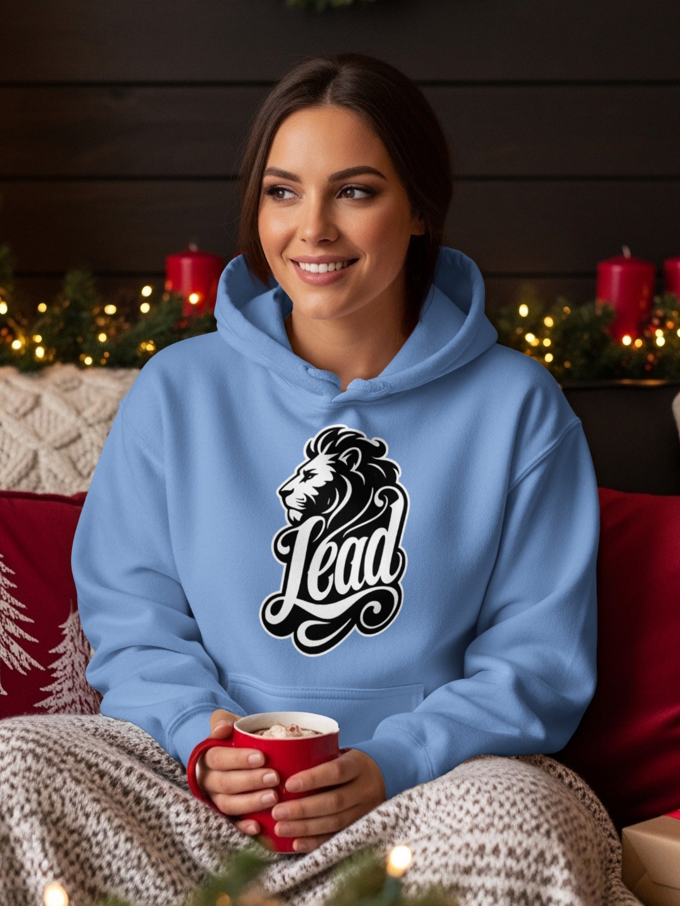 Light blue hoodie with lion and "Lead" graphic, held by a woman with a mug.