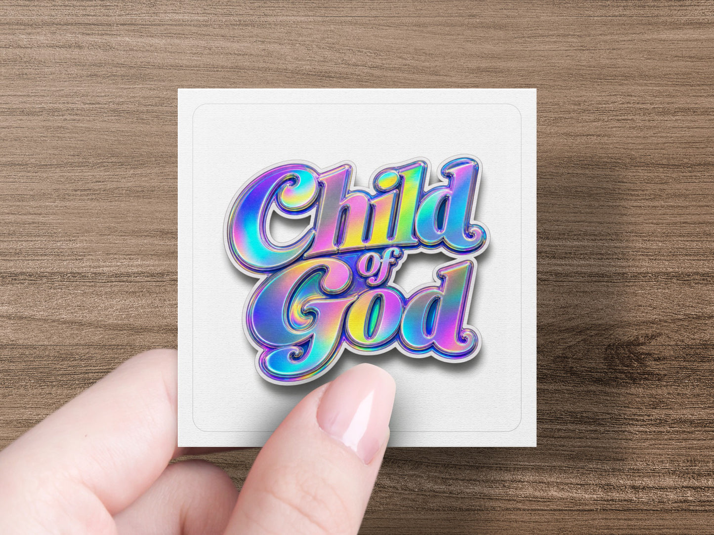"Child of God" text with iridescent colors on a white square card held by a hand.