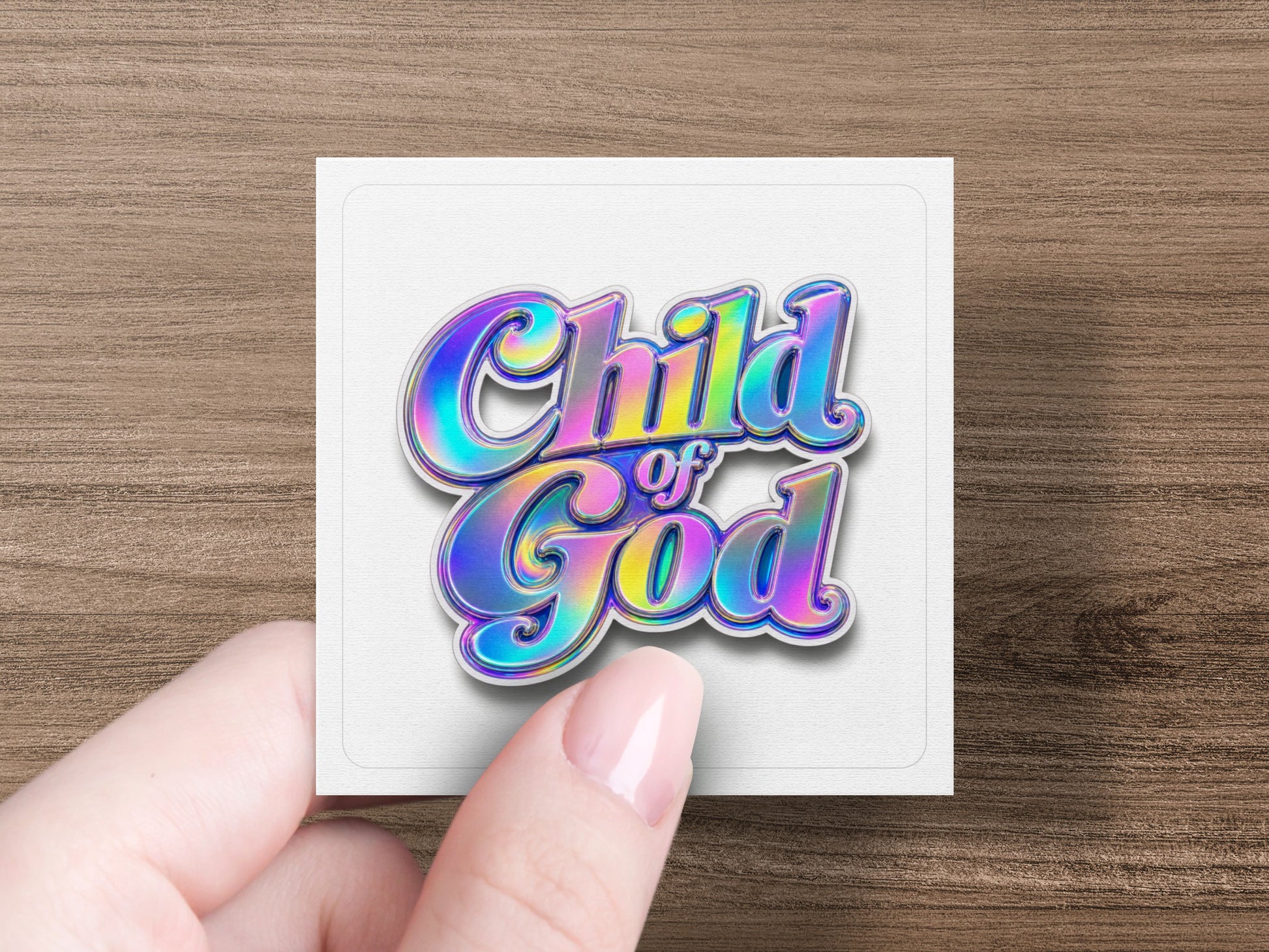 "Child of God" text with iridescent colors on a white square card held by a hand.
