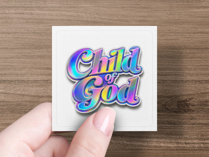 "Child of God" text with iridescent colors on a white square card held by a hand.