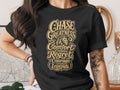 Black t-shirt with gold text and a lion graphic that reads "Chase Greatness Comfort Creates Regret Courage Creates Legends."