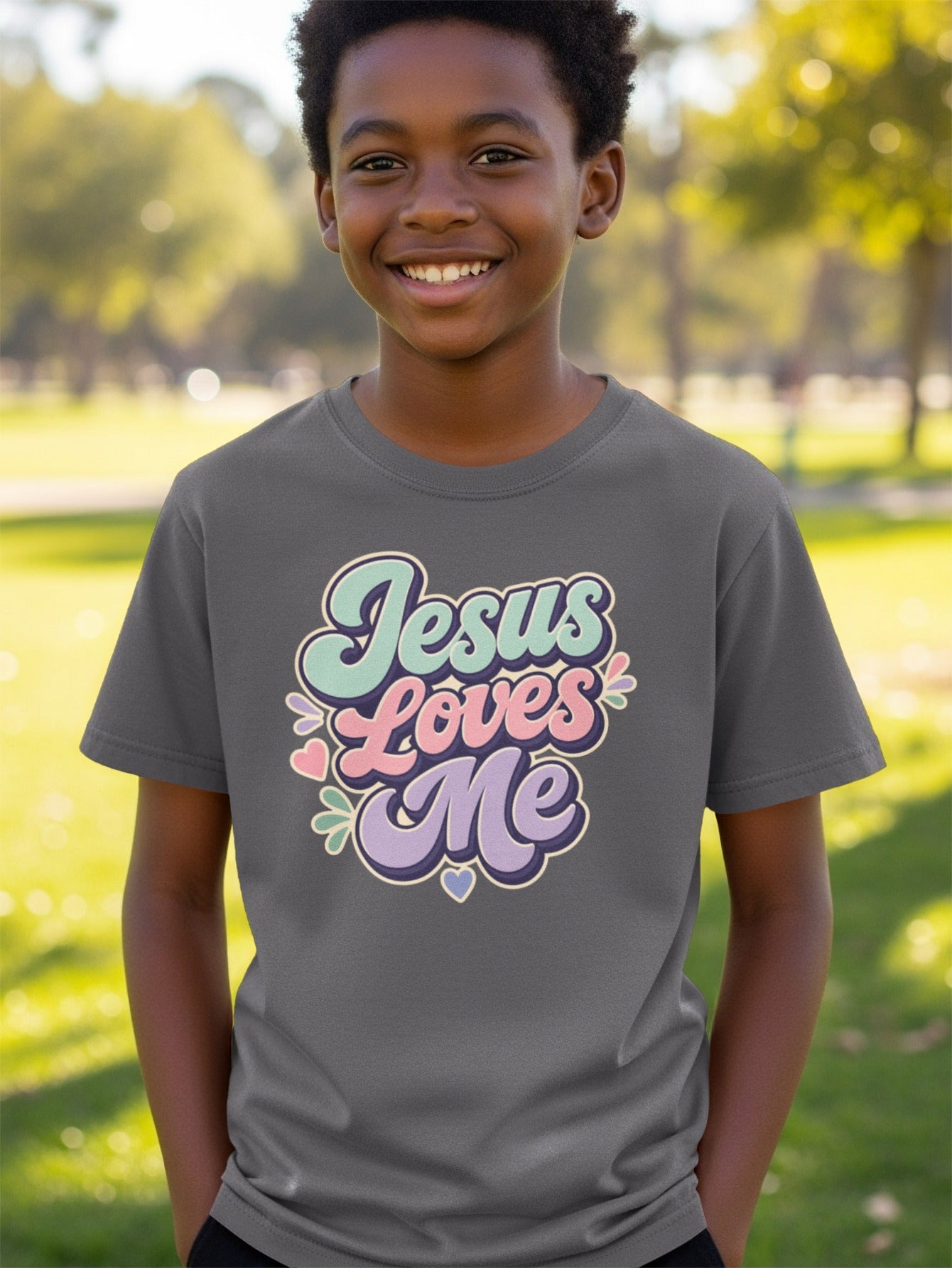 Boy wearing dark gray t-shirt with pastel "Jesus Loves Me" text and hearts.