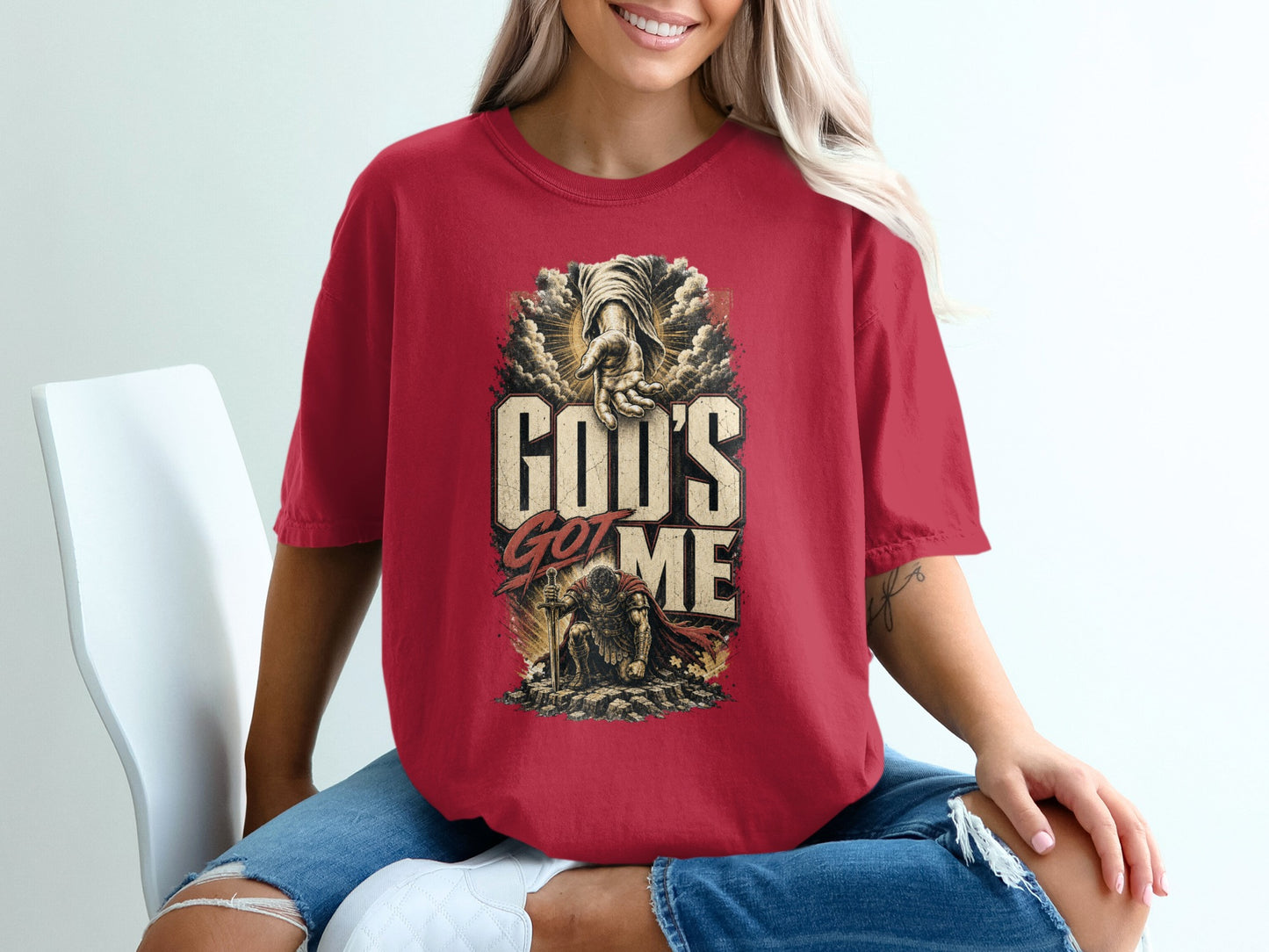 Red t-shirt with graphic displaying "God's Got Me" and a kneeling armored man.