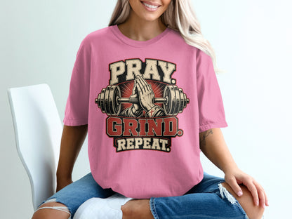 Pink t-shirt with "Pray. Grind. Repeat." text and praying hands between a barbell.