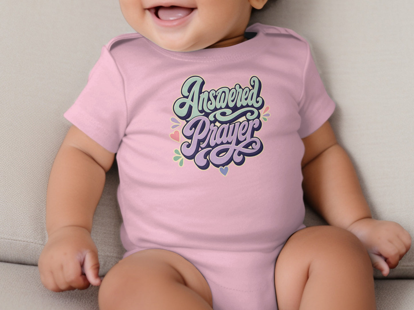 Pink toddler onesie with "Answered Prayer" text and pastel heart accents.