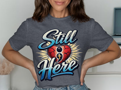 Gray t-shirt with "Still Here" text, cracked heart, and cross.
