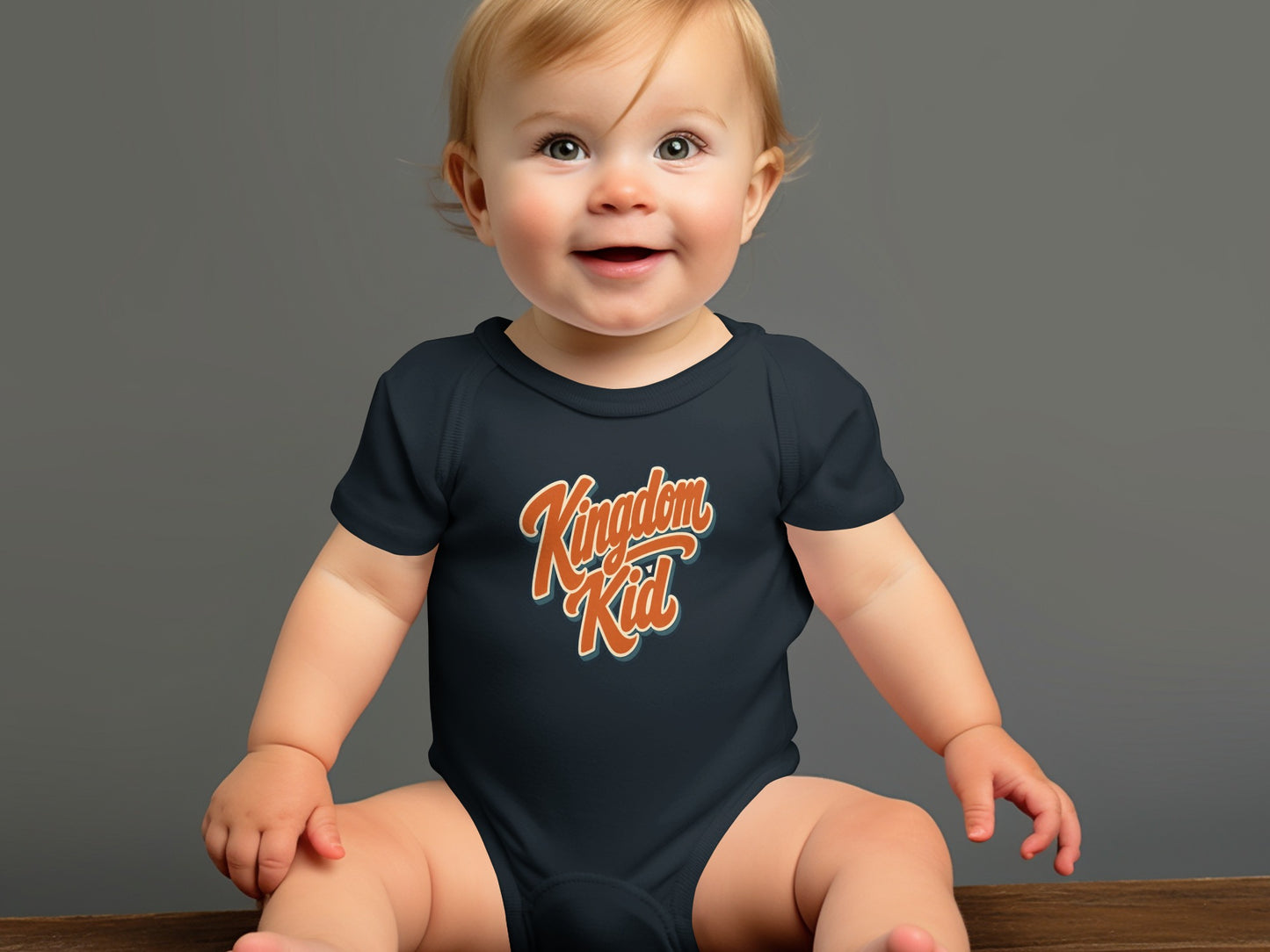 Baby wearing dark blue bodysuit with orange "Kingdom Kid" text.