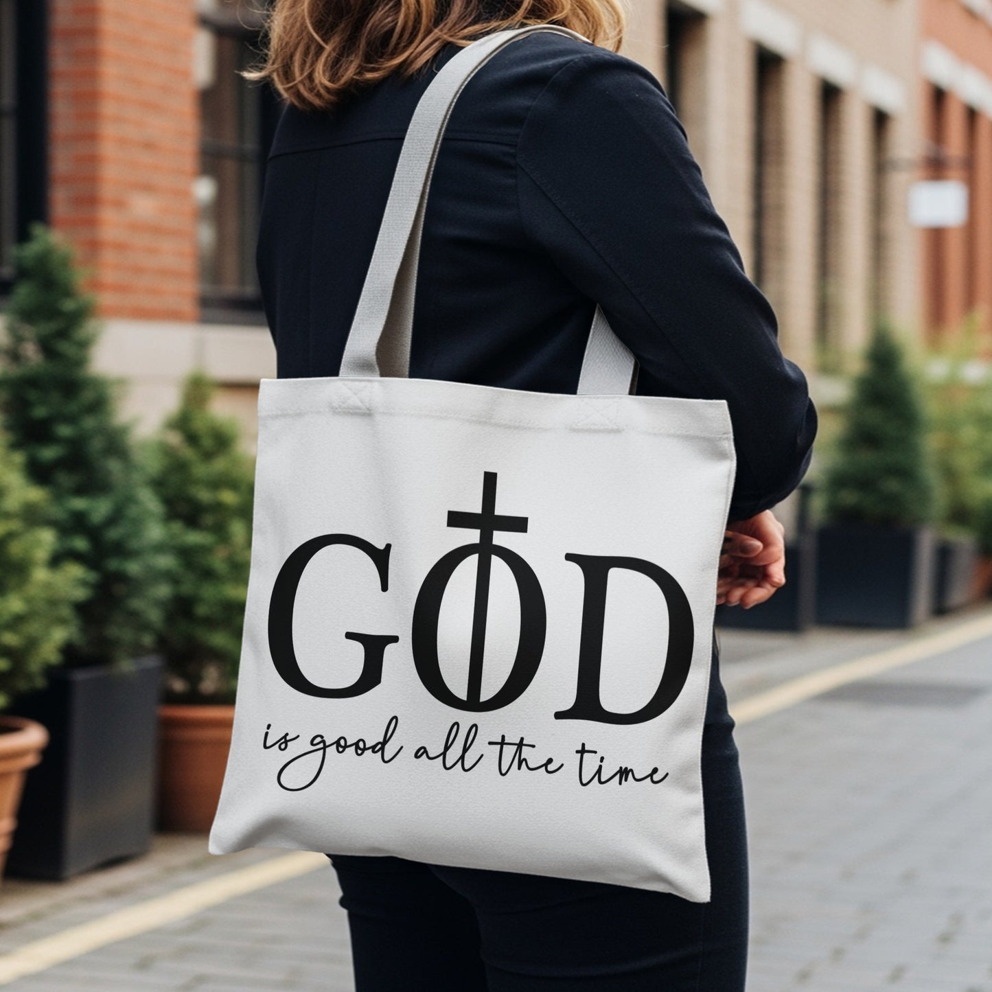White tote bag with black text "GOD is good all the time" and cross symbol.