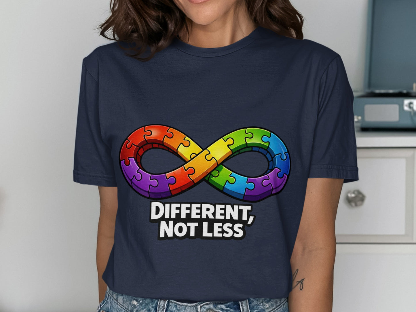 Navy t-shirt with rainbow infinity puzzle piece symbol and "DIFFERENT, NOT LESS" text.