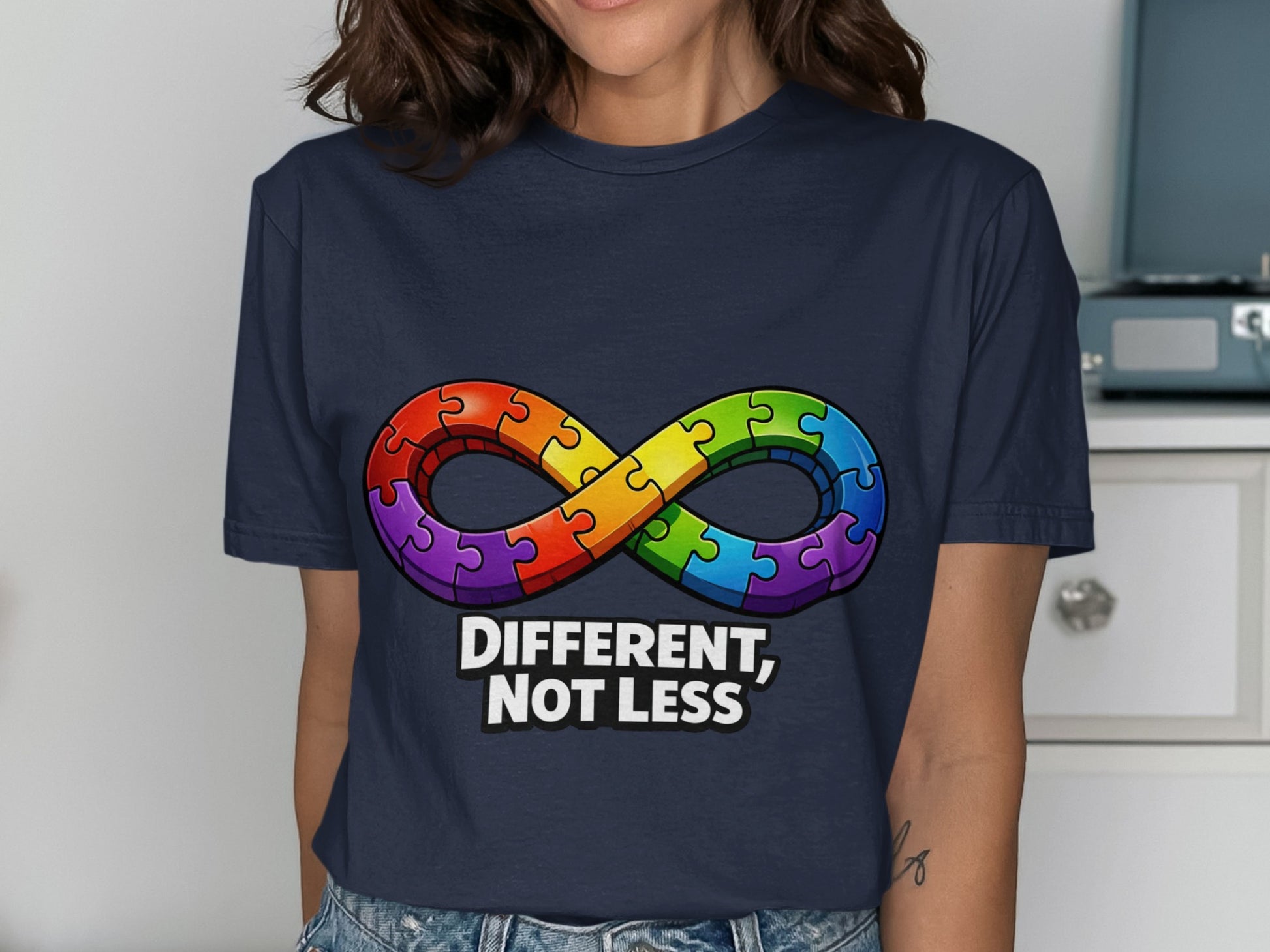 Navy t-shirt with rainbow infinity puzzle piece symbol and "DIFFERENT, NOT LESS" text.