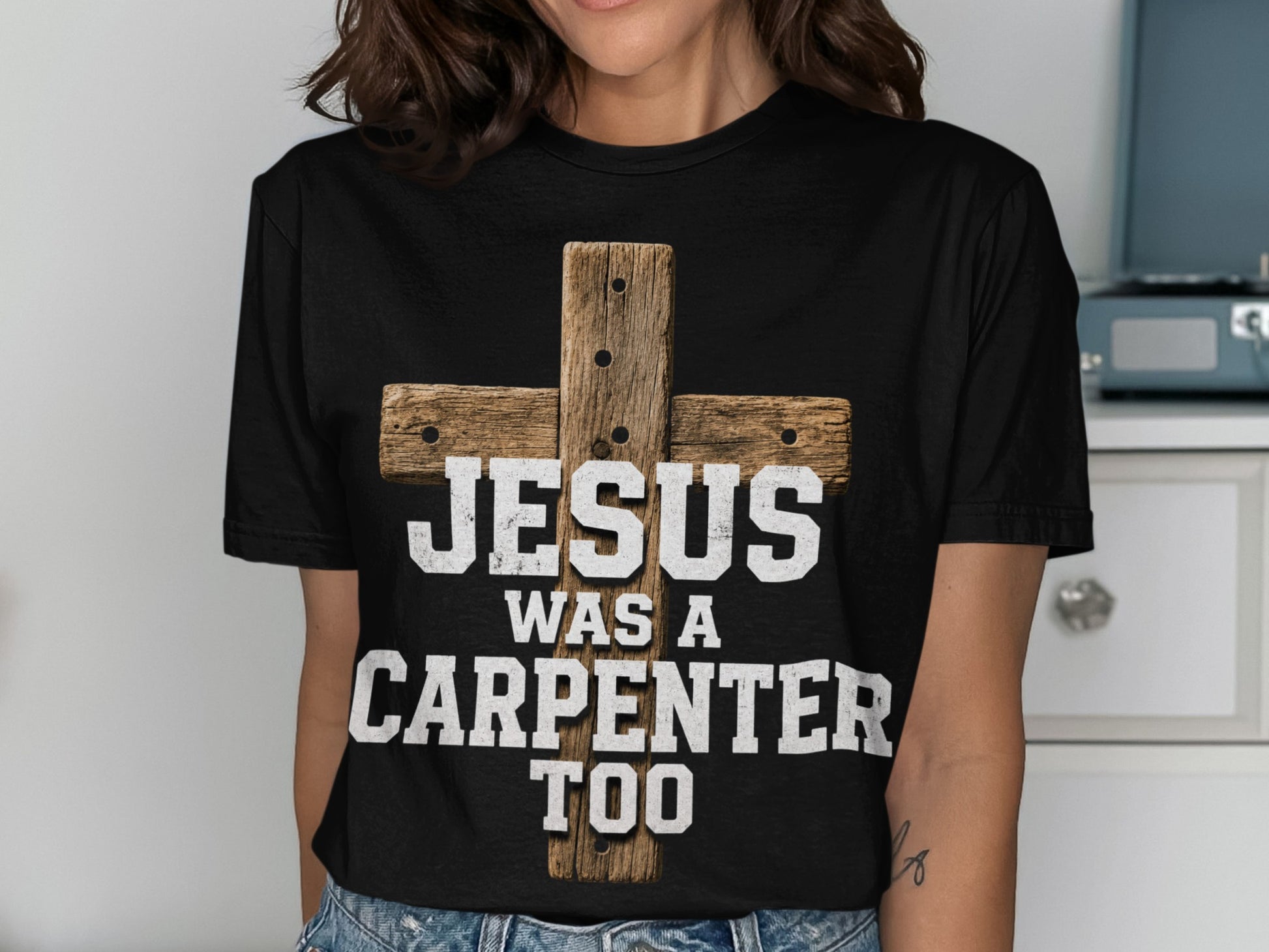 Black t-shirt with a rustic wooden cross and text reading "JESUS WAS A CARPENTER TOO".