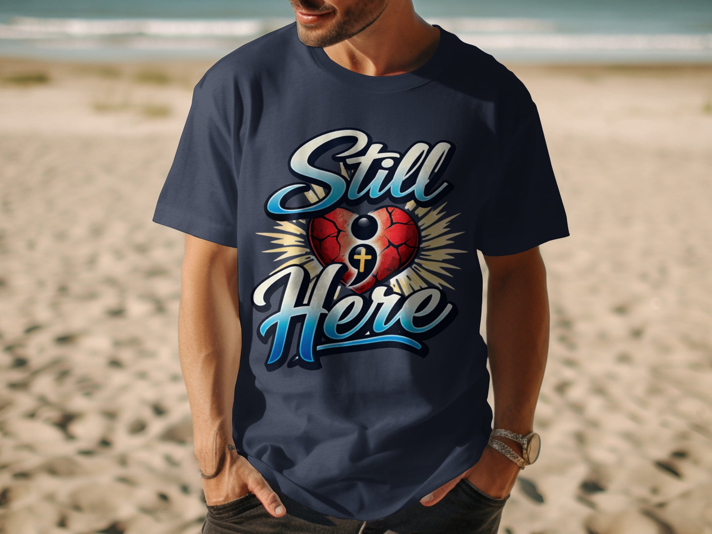 Navy t-shirt with "Still Here" text and a heart with a cross graphic.
