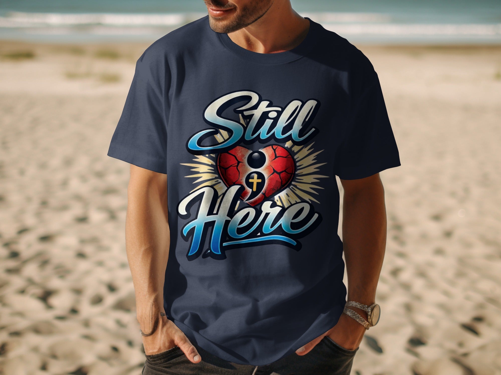 Navy t-shirt with "Still Here" text and a heart with a cross graphic.