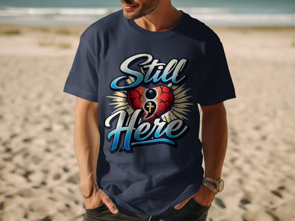 Navy t-shirt with "Still Here" text and a heart with a cross graphic.
