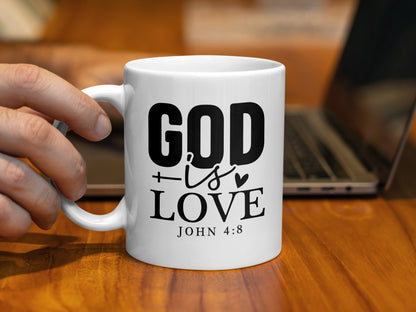 White mug with black text "GOD is LOVE JOHN 4:8" held by a hand.