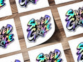 Holographic sticker with "SAVED BY GRACE" text on a wooden background.