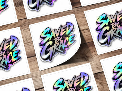 Holographic sticker with "SAVED BY GRACE" text on a wooden background.