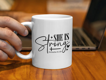White mug with black text reading "SHE IS Strong" and "Proverbs 31:25."