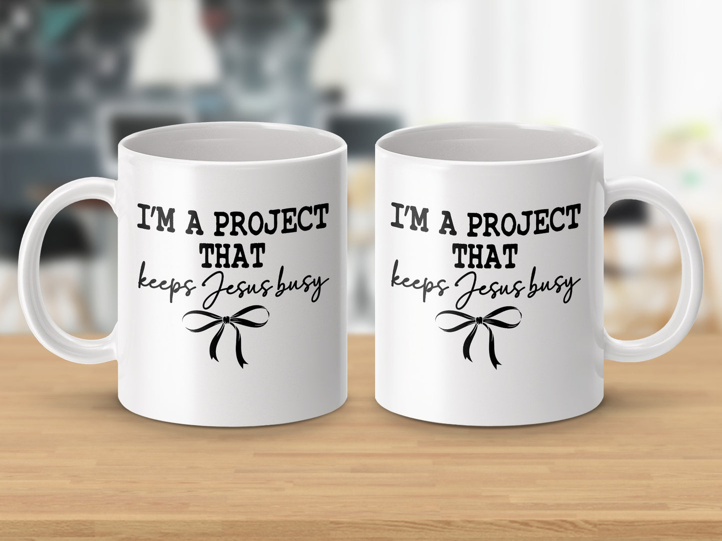 Two white mugs with black text reading "I'm a project that keeps Jesus busy."