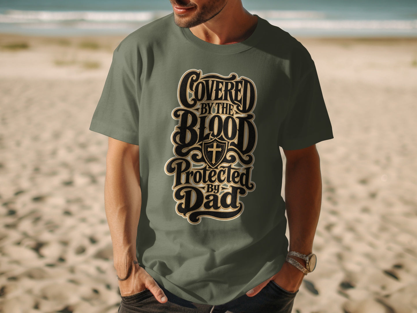 Green t-shirt with text "COVERED BY THE BLOOD PROTECTED BY DAD" and a cross shield.