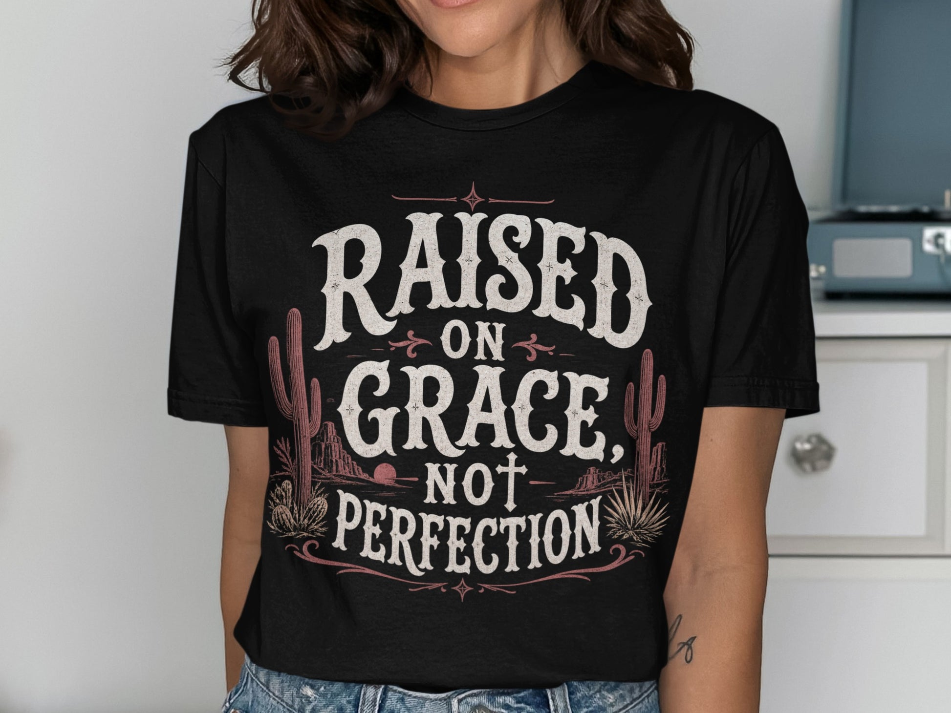Black t-shirt with "Raised on Grace, Not Perfection" text and desert graphics.
