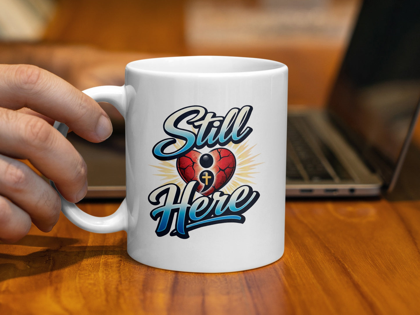 White mug with "Still Here" text and a cross inside a broken heart.