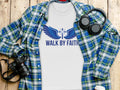 White t-shirt with blue wings and cross graphic, text "WALK BY FAITH".