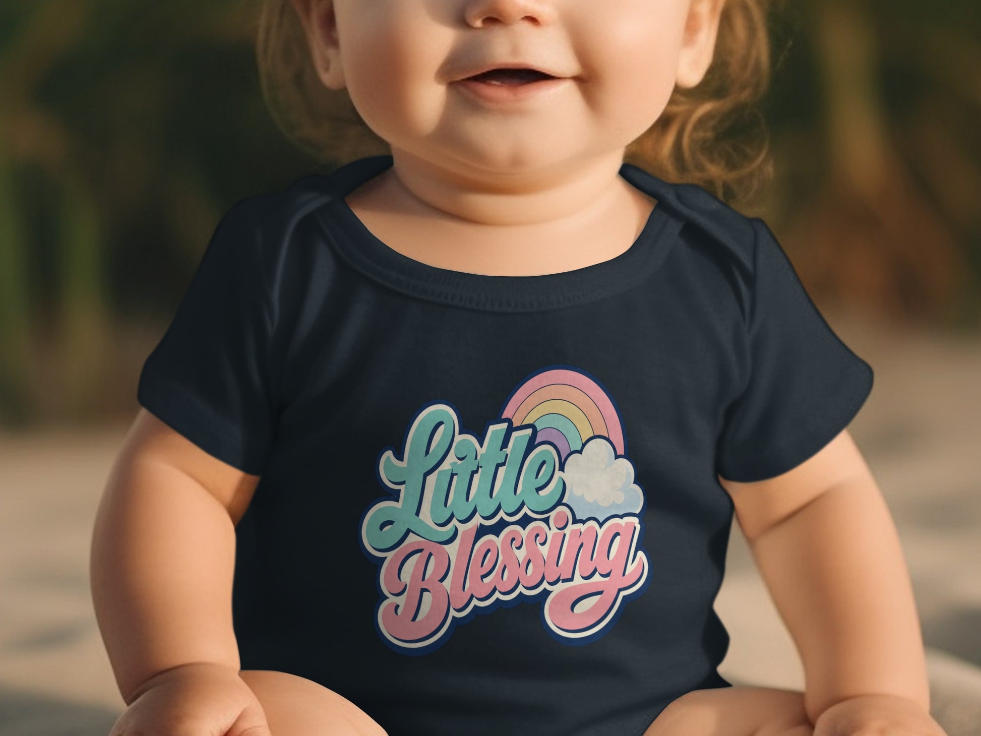 Baby in navy onesie with "Little Blessing" text and rainbow graphic.
