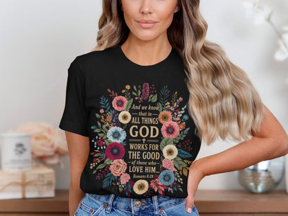 Black t-shirt with floral wreath and text "God works for the good... Romans 8:28".