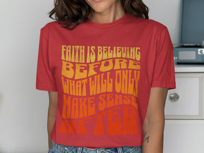 Red t-shirt with yellow and orange text reading "FAITH IS BELIEVING BEFORE WHAT WILL ONLY MAKE SENSE AFTER"