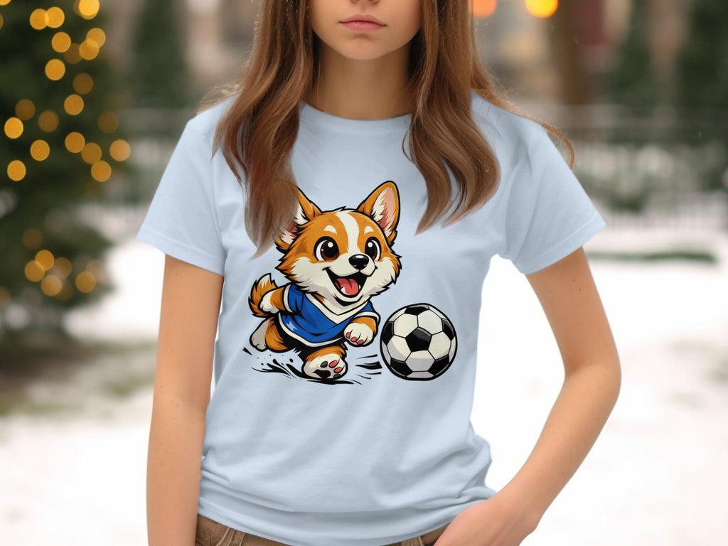 Corgi wearing soccer jersey kicks a soccer ball on a light blue t-shirt.