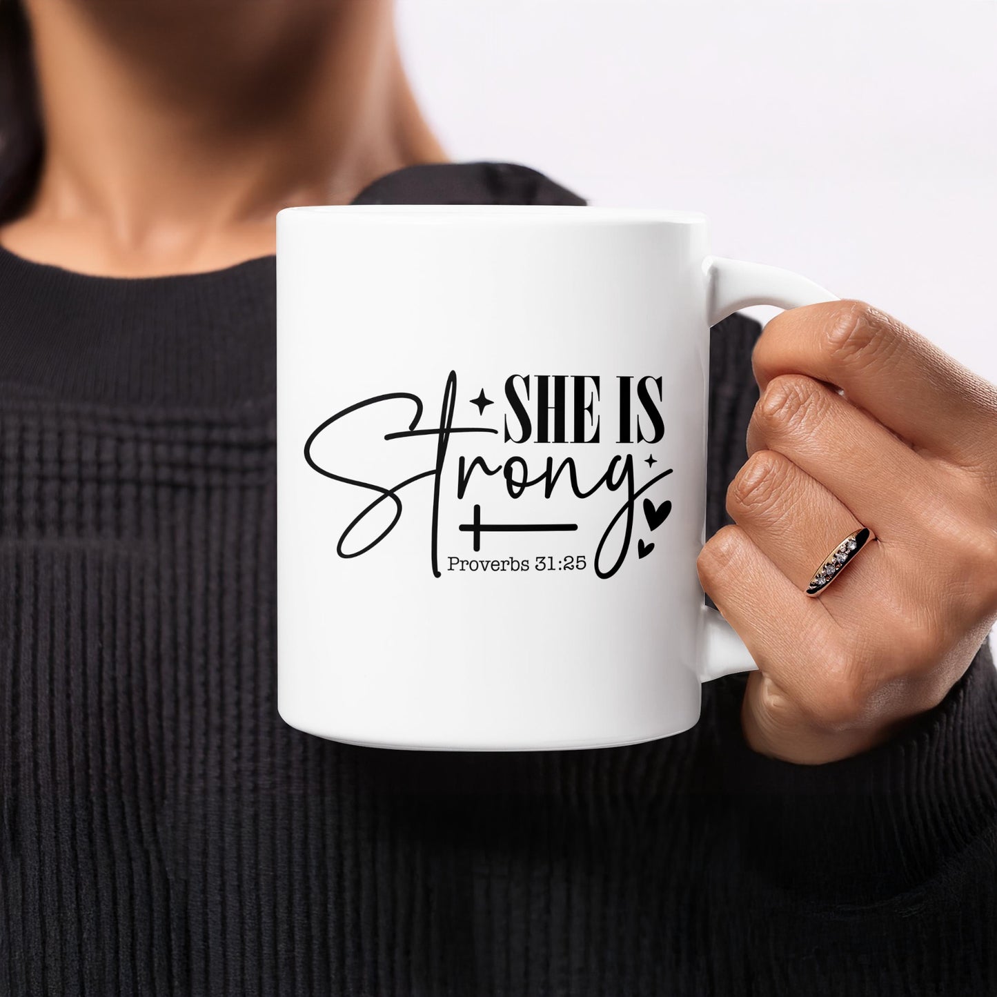 White mug with black text "SHE IS Strong" and "Proverbs 31:25".