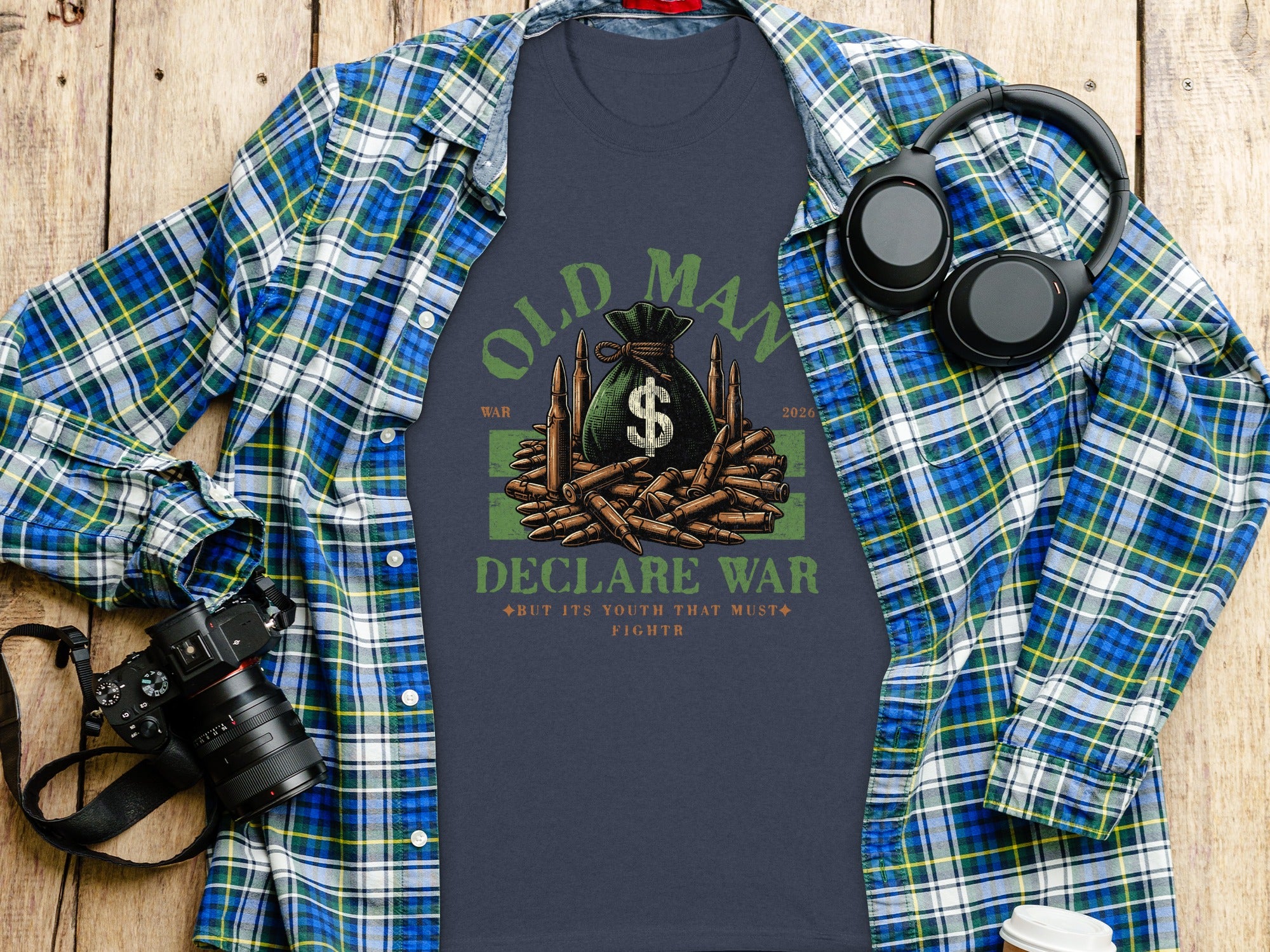 Dark t-shirt with "Old Man Declare War" text, money bag, bullets, and headphones on a wooden background.