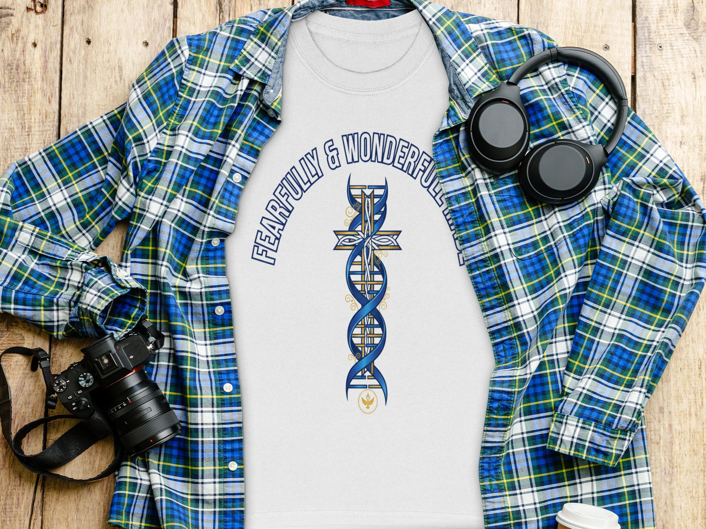 White t-shirt with "Fearfully & Wonderful" text and DNA cross graphic, laid flat with plaid shirt.