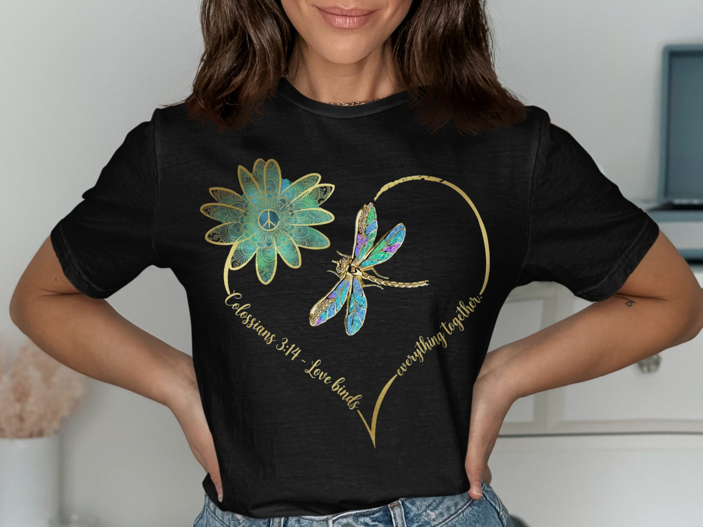 Black t-shirt with gold heart outline, dragonfly, flower, and text "Colossians 3:14 - Love binds everything together."