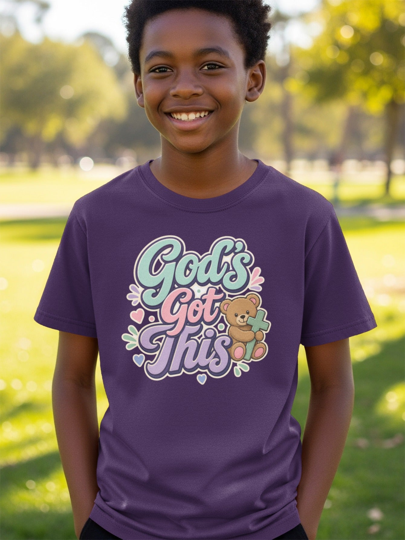 Boy wearing purple t-shirt with "God's Got This" text, teddy bear, and cross graphic.